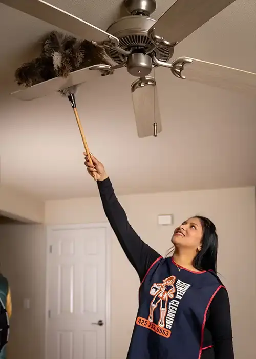 A photo of an Esthela cleaner stretching to dust a cieling fan
